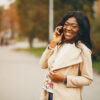 Elegant black woman standing in a autumn city. Businesswoman in a long coat. Lady use the phone